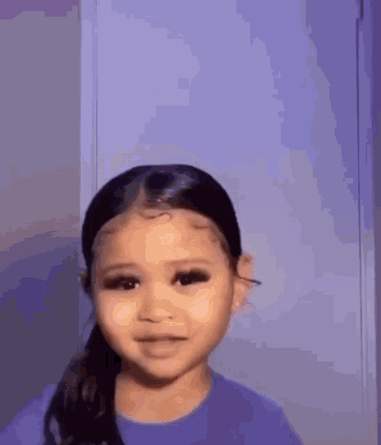 a little girl in a purple shirt is standing in front of a purple wall .