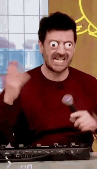 a man wearing a red sweater is holding a microphone and making a funny face