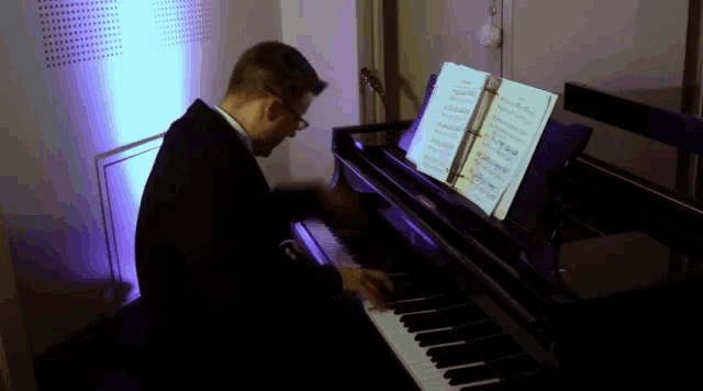 a man in a suit is playing a piano with a sheet of music on it