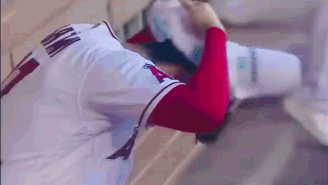 a baseball player wearing a white jersey and red sleeves is holding a bottle of water in his hand .