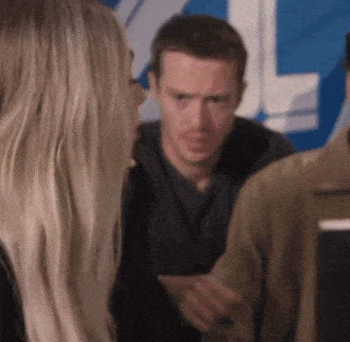 a man and a woman are talking to each other in front of a blue sign .