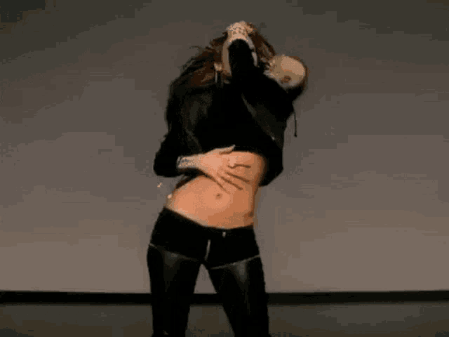 a woman in a black crop top and leather pants is dancing in a room .