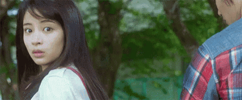a woman is looking over her shoulder at a man in a plaid shirt in a park .