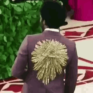 a man in a purple suit with a gold all seeing eye on the back of his jacket .