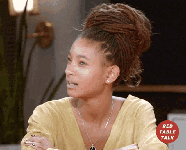 a woman with dreadlocks is sitting in front of a red table talk logo