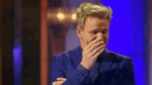 a man in a suit is covering his mouth with his hands while laughing .