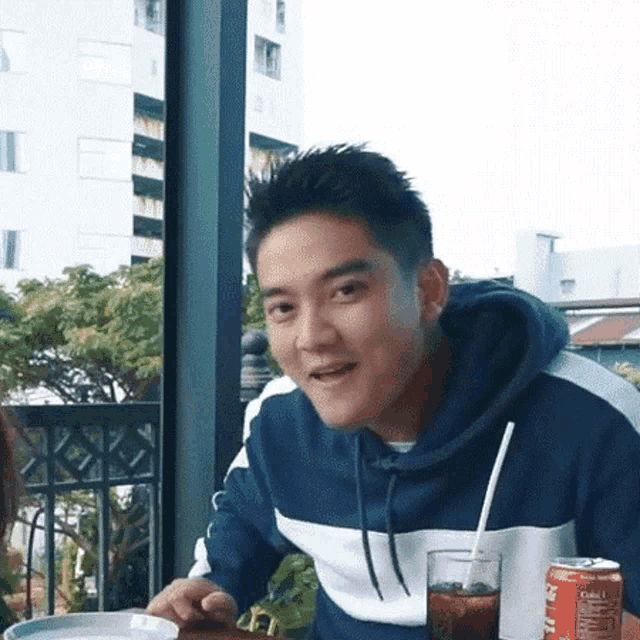 a young man is sitting at a table with a can of soda and a glass of cola .