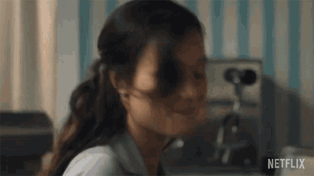 a close up of a woman 's face in a kitchen with a striped wall behind her .