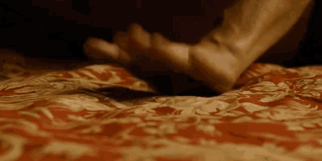 a person 's hand is laying on a bed with a red and white blanket .