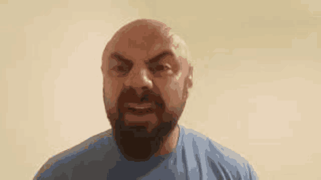 a bald man with a beard is wearing a blue shirt and making an angry face .