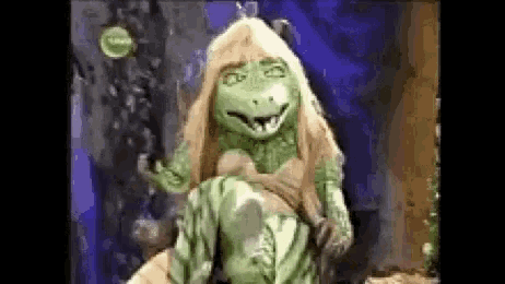 a green frog with long blonde hair is sitting on a rock in a cave .