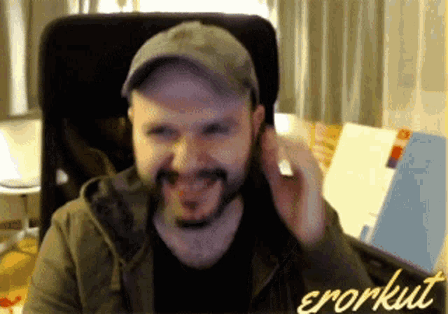a man with a beard wearing a hat is sitting in a chair with errorkut written on the bottom right
