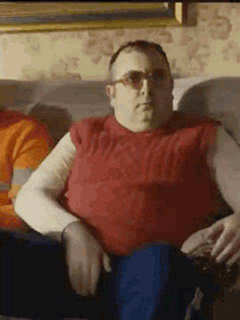 a man is sitting on a couch wearing sunglasses and a red sweater .