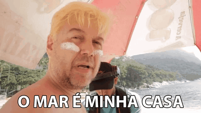 a shirtless man stands under an umbrella with the words o mar e minha casa written below him