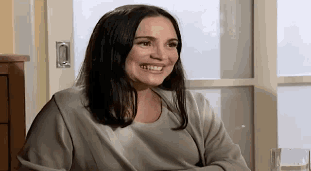 a woman is smiling and sitting in front of a window .