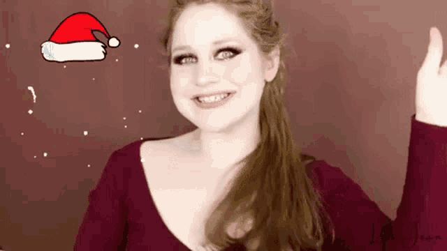 a woman wearing a santa hat is smiling in front of a red background