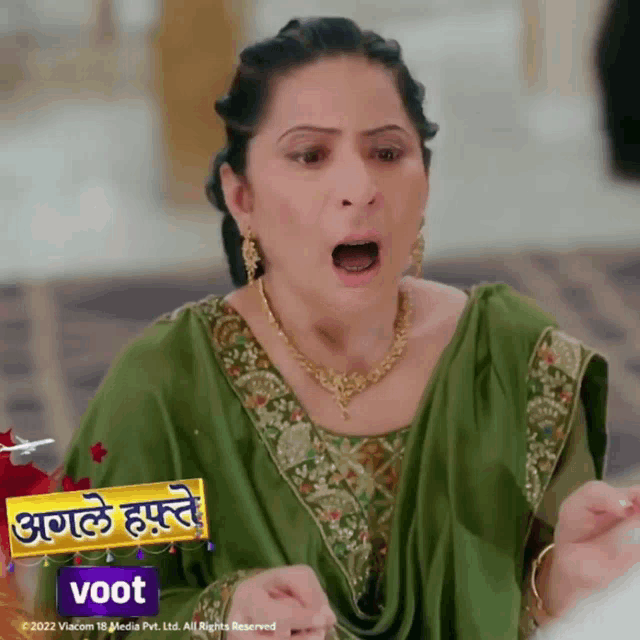 a woman in a green dress is making a funny face in front of a voot ad