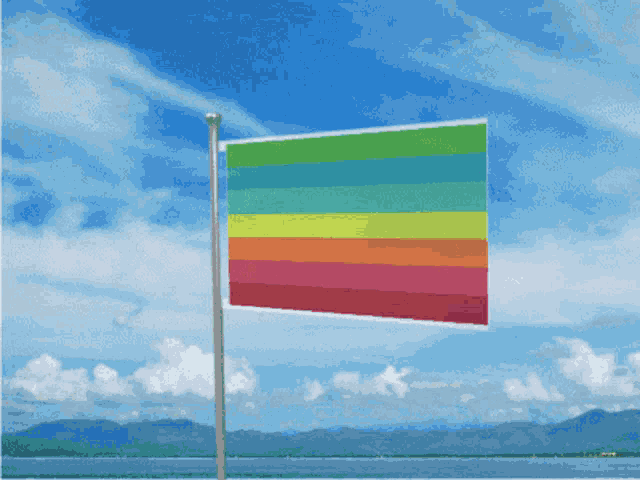 a rainbow flag is flying in the wind in front of a blue sky