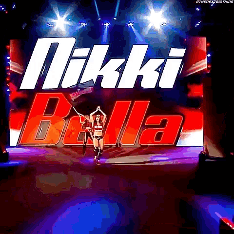 a woman is walking on a stage in front of a large screen that says " nikki bella "