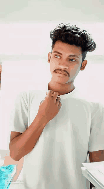 a young man with a mustache is wearing a white t-shirt and looking at the camera
