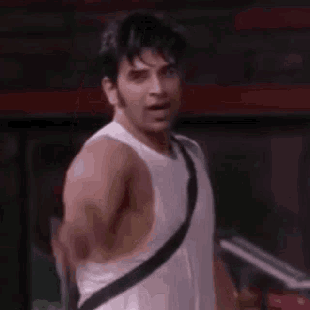 a man in a white tank top is pointing at the camera with a gun in his hand .