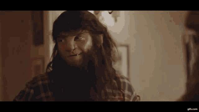 a man with long hair and a beard is looking at himself in the mirror .