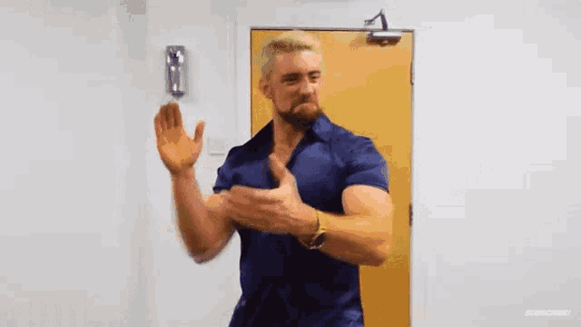 a man in a blue shirt is clapping his hands in front of a yellow door .