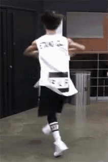 a man in a white tank top and black shorts is running in a gym .