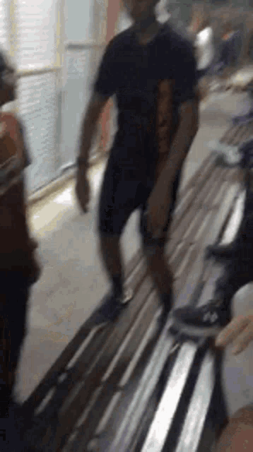 a man in a black shirt and shorts is standing next to a bench .