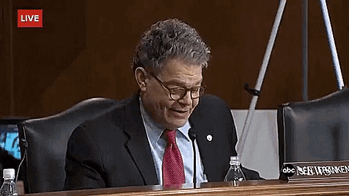 a man in a suit and tie sits at a table with a name plate that says robert franken on it