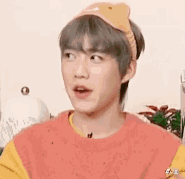 a young man wearing a yellow headband and a pink sweater is making a surprised face .
