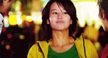 a woman wearing a yellow jacket and a green shirt is standing in a crowd .