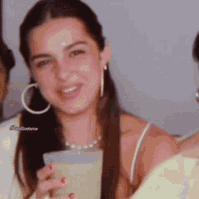 a woman wearing hoop earrings is holding a drink in her hand .