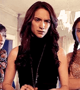 a woman in a black tank top and a necklace is standing next to two other women .