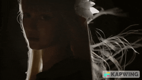 a woman with a flower in her hair is in a dark room with the word kapwing in the corner