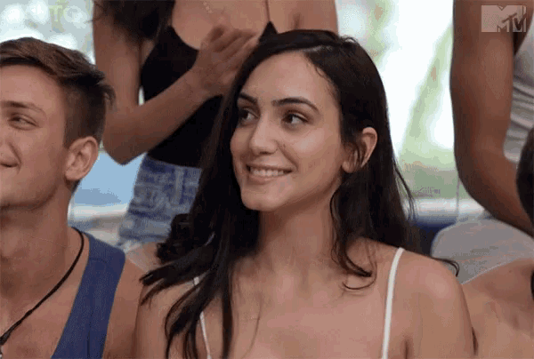 a woman in a white tank top smiles in front of a group of people with a mtv logo in the corner