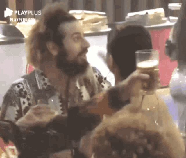 a man with a beard is holding a glass of beer while talking to a woman .
