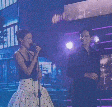 a woman sings into a microphone while a man stands behind her