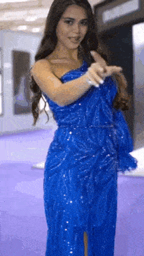 a woman is wearing a blue dress and pointing at the camera .