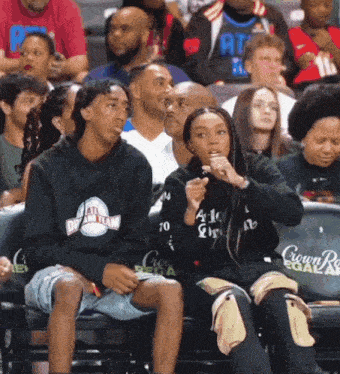 a group of people sitting in a stadium with one wearing an atl dream team shirt