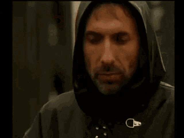 a man with a beard is wearing a black hooded jacket and looking at the camera .