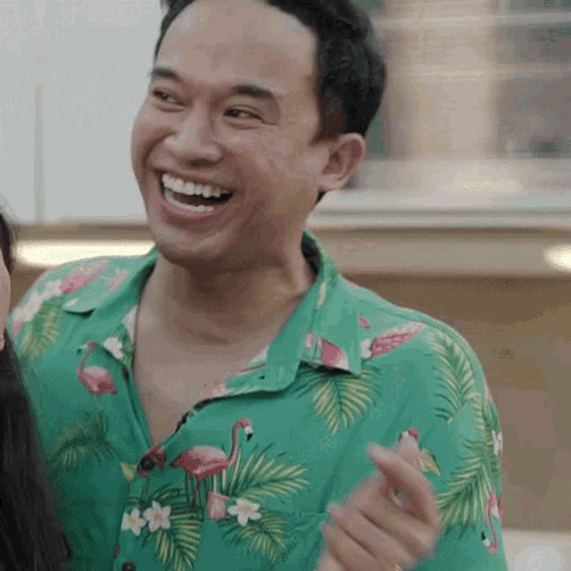 a man wearing a green shirt with flamingos on it laughs