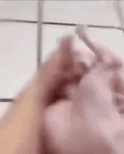a close up of a person 's hand holding something in front of a white tiled wall .