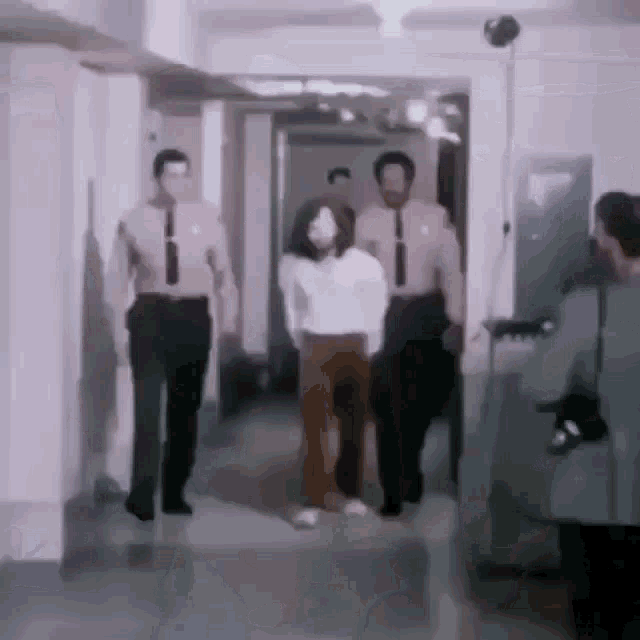 a group of people are walking down a hallway and one of them is wearing a white shirt and brown pants .