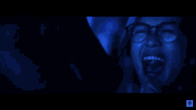 a woman wearing glasses is smiling in a dark room with blue lights
