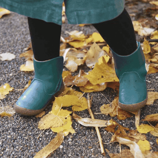 a child wearing a pair of green boots is standing on a pile of leaves