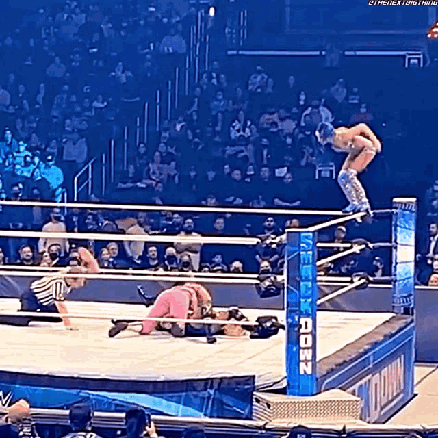 a wrestler is jumping over another wrestler in a wrestling ring with a sign that says ' wwe '