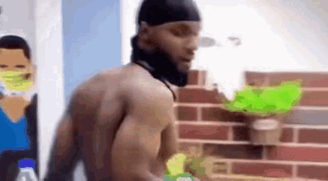 a man without a shirt is standing in front of a brick wall .