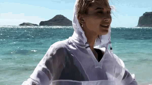a woman wearing a white hoodie is standing on a beach