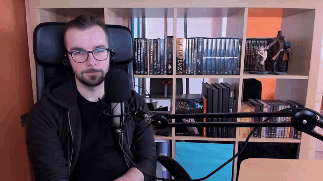 a man sitting in front of a microphone with a bookshelf behind him that says twin peaks